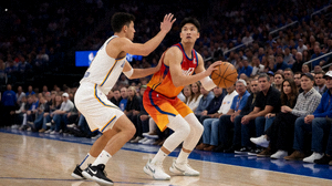NBA常规赛比赛现场，球员在三分线外准备投篮，防守球员紧贴，观众席气氛热烈