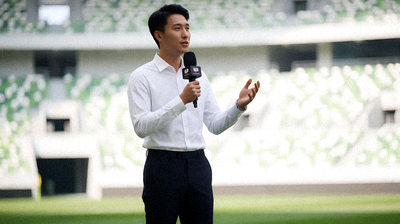 体育新闻记者正在赛场边采访报道，镜头前有麦克风设备